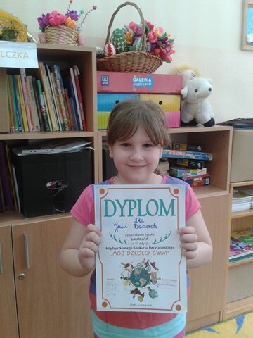 Zdjęcie przedstawia laureatkę Międzyszkolnego Konkursu Recytatorskiego. Uczennica na tle szkolnych mebli pozuje do zdjęcia z uzyskanym dyplomem. 