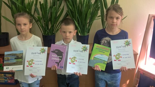 Zdjęcie trojga uczniów prezentujących otrzymane dyplomy i nagrody książkowe.