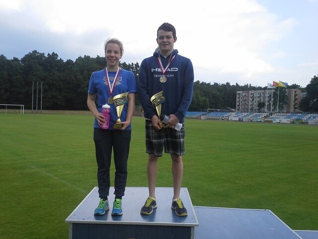 Zdjęcie dwojga uczniów na podium. Zwycięzcy prezentują medale i puchary.