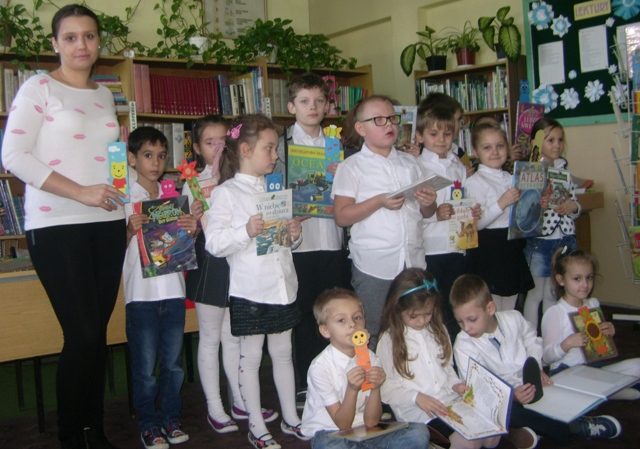 Zdjęcie przedstawiające uczniów w bibliotece szkolnej po pasowaniu na czytelnika. Dzieci prezentują książki.