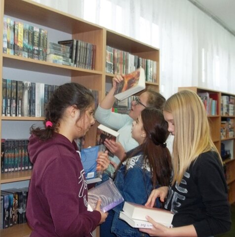 Uczniowie wybierają książki z regałów bibliotecznych.