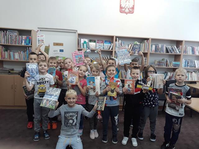 Zdjęcie przedstawia uczniów w bibliotece szkolnej. Dzieci prezentują książki.