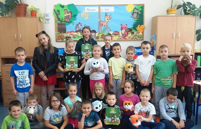 Zdjęcie przedstawiające uczniów w sali lekcyjnej. Kilkoro dzieci prezentuje książki lub maskotki. 