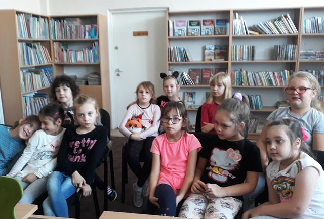 Zdjęcie prezentujące uczennice podczas zajęć w bibliotece szkolnej. W tle regały z książkami.