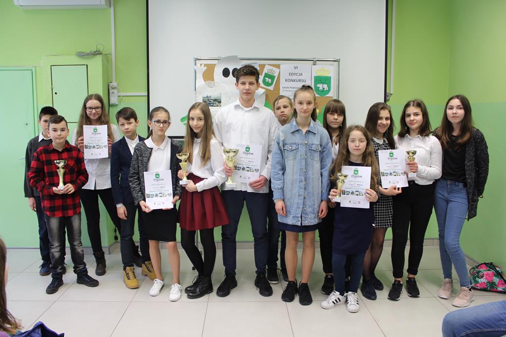 Grupa uczniów i nauczycieli  podczas podsumowania konkursu „O Chełmie wiedzą wszystko”. Uczniowie prezentują nagrody.