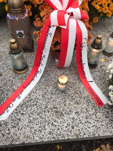 Zdjęcia nagrobka z zapalonymi zniczami i złożonymi wieńcami