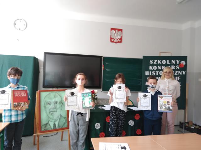 Zdjęcie laureatów konkursu z nauczycielem. Uczniowie trzymają w rękach dyplomy i nagrody książkowe.
