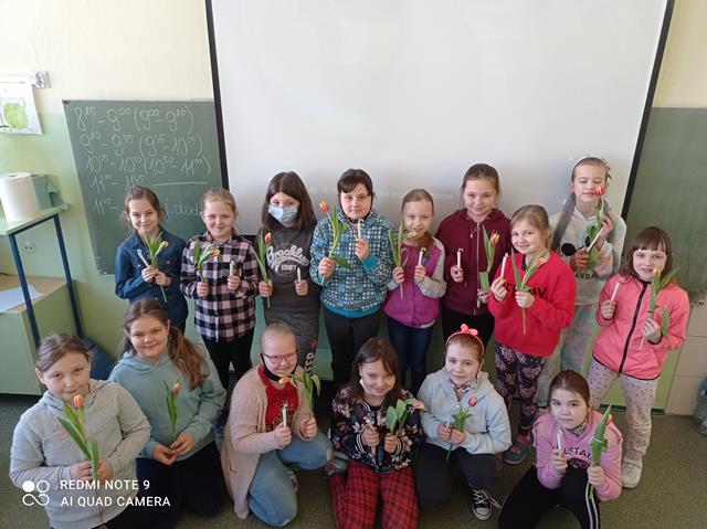 Grupa dziewcząt z kwiatami i upominkami z okazji Dnia Kobiet.