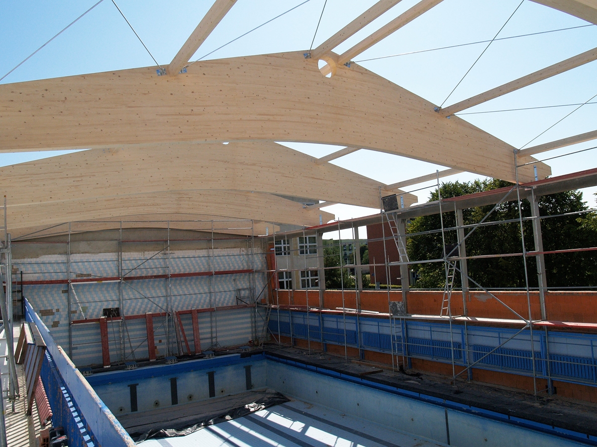 Zdjęcie przedstawiające wnętrze hali basenu podczas budowy – nowe elementy zadaszenia pływalni.