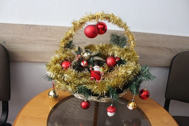 Zdjęcie przedstawia świąteczny stroik z czerwonymi bombkami i złotym łańcuchem.