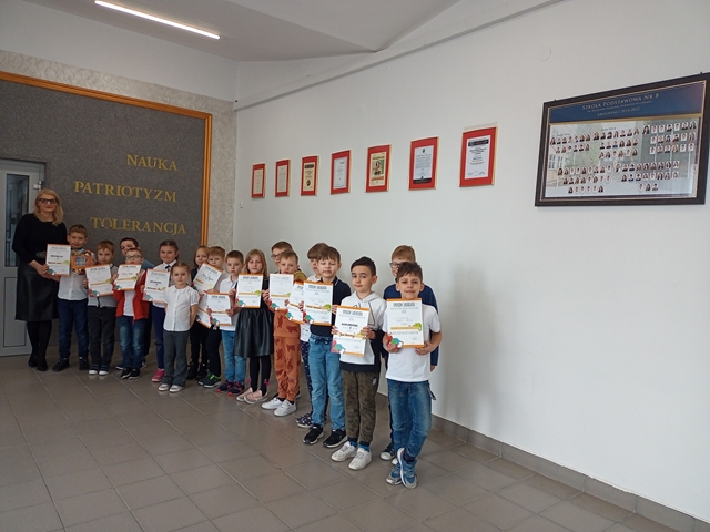 Pani Dyrektor wraz z grupą laureatów ogólnopolskiego konkursu przedmiotowego Leon. Uczniowie trzymają przed sobą dyplomy.